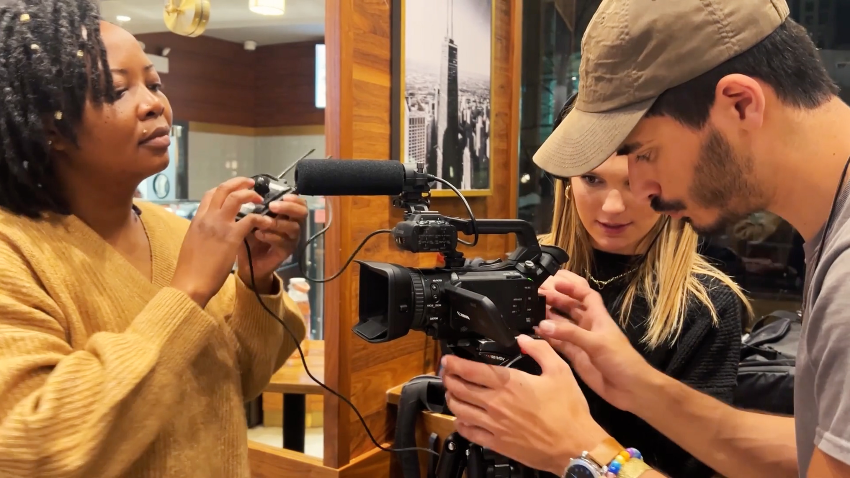 Three people adjust camera equipment in a dark restaurant.