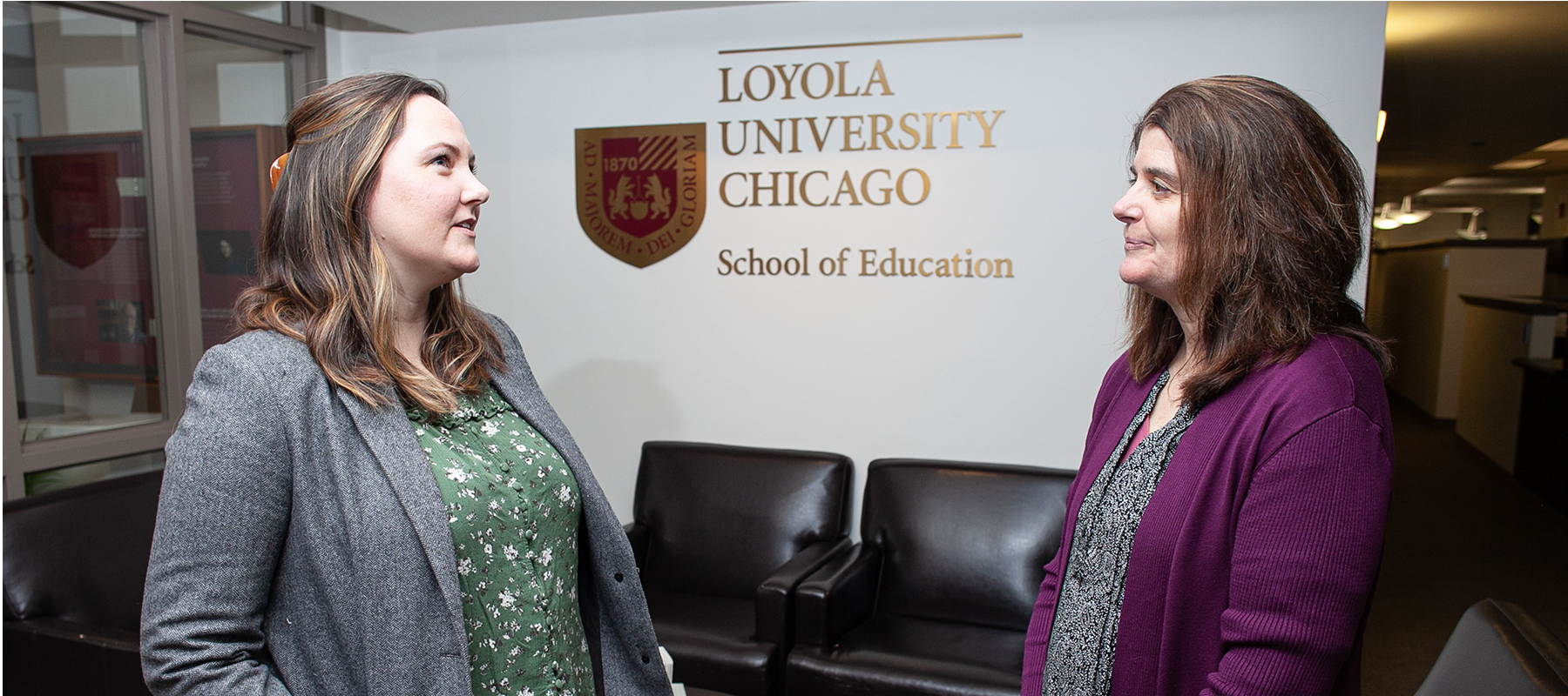 Two faculty members speak in the School of Education office.