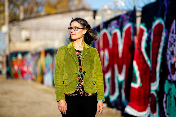 Photo of a woman wearing a bright green jacket standing in front of a graffiti wall